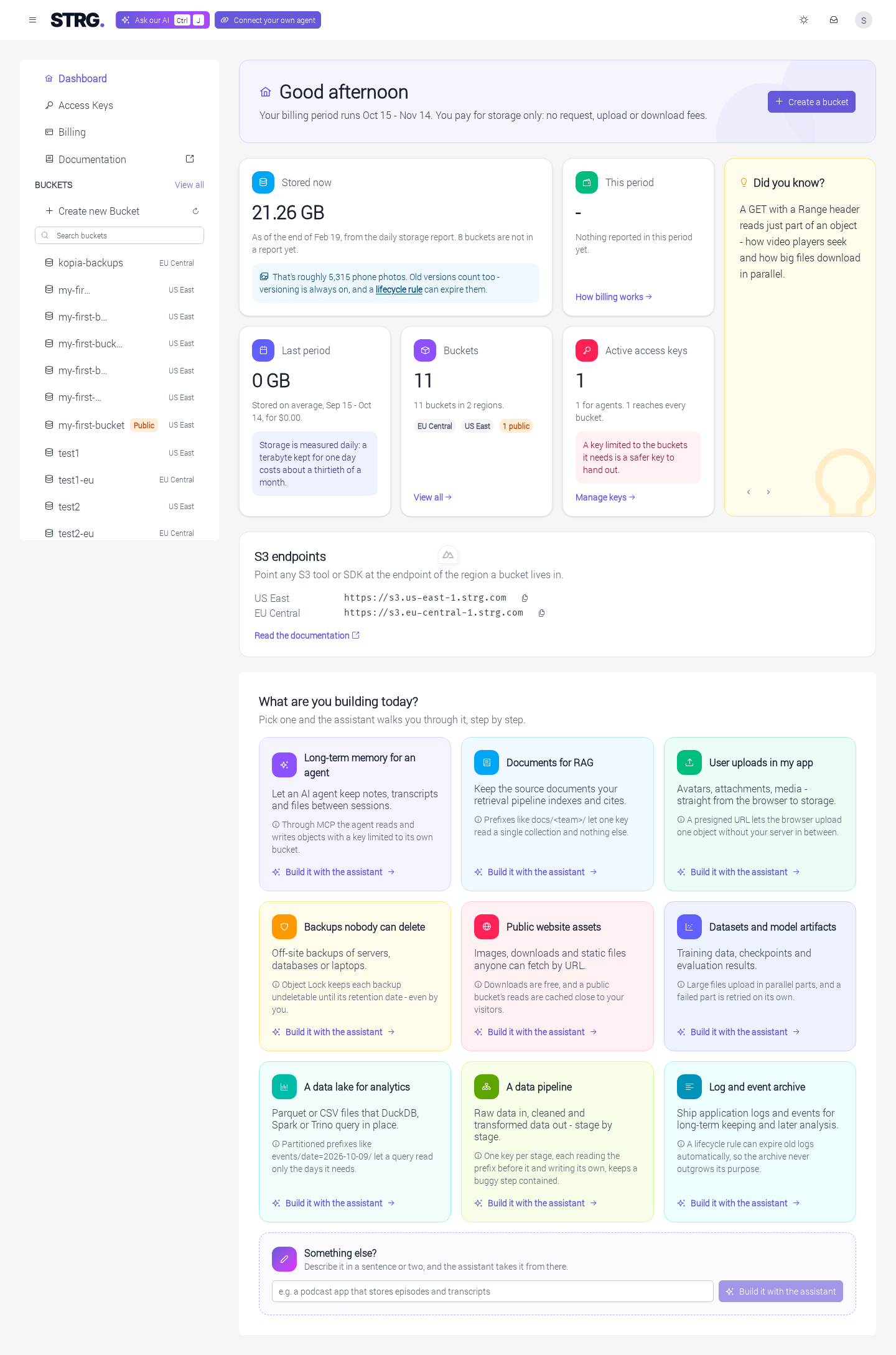 The dashboard: the top bar with the "Ask our AI" button, showing its keyboard shortcut, and the "Connect your own agent" button beside the STRG mark; the sidebar listing Dashboard, Access Keys, Billing, Documentation and a Buckets section with a "View all" link, "Create new Bucket" with a refresh button and a search field above the bucket list; and the Dashboard page with a greeting, a "Create a bucket" button, and the Stored now, This period, Last period, Buckets, Active access keys and Did you know? tiles above an S3 endpoints card with a copy button per region